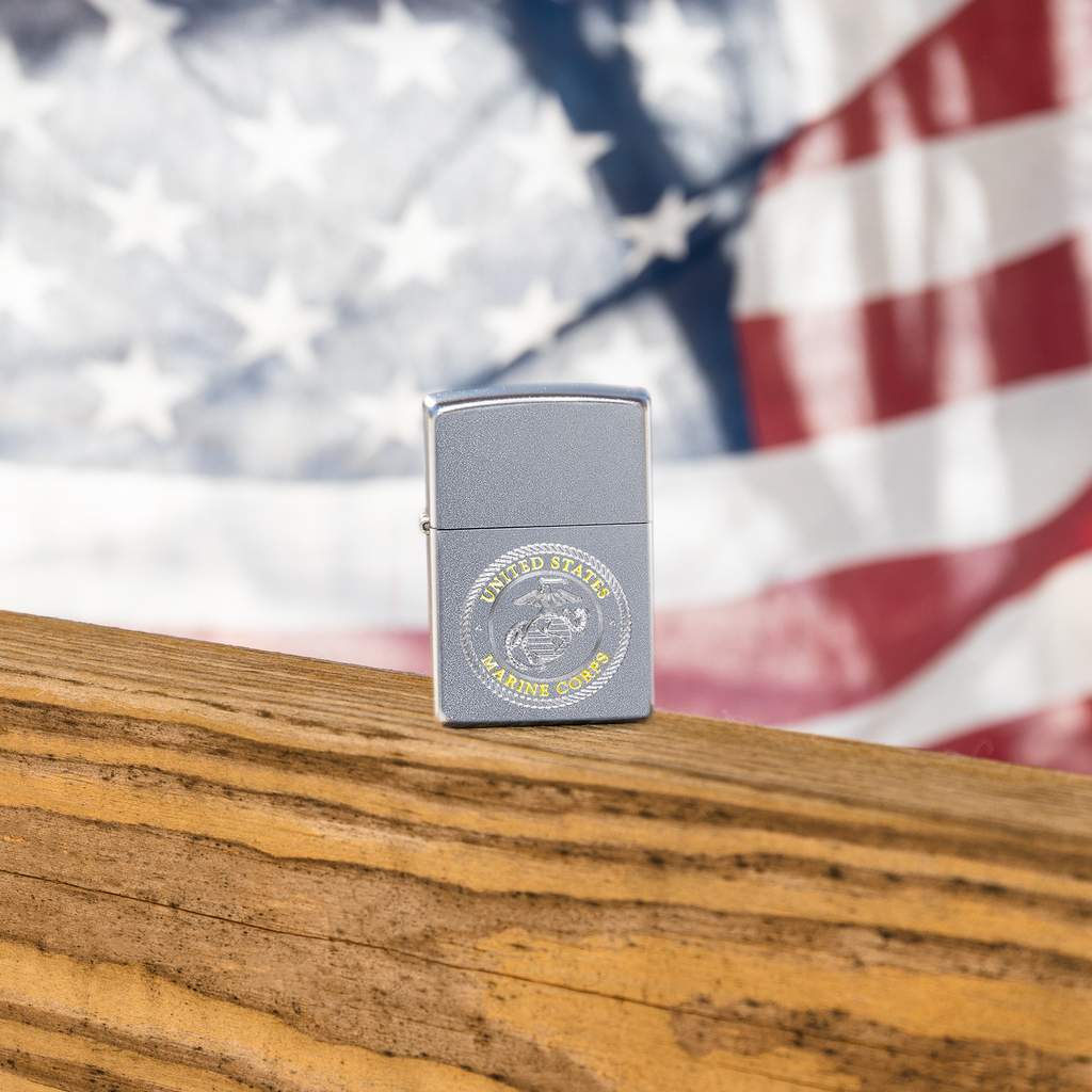 Lifestyle image of U.S. Marines Corps. Crest Windproof Lighter with the American Flag in the background