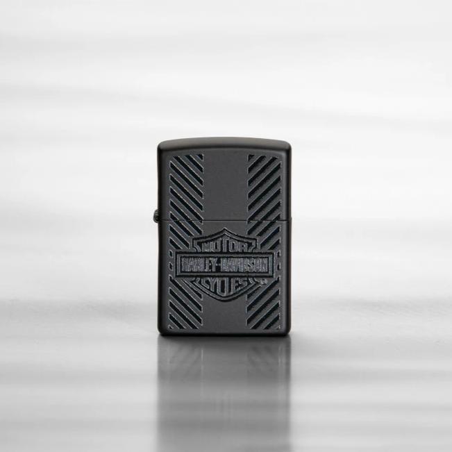 Lifestyle image of Harley-Davidson® Classic Logo Black Matte Windproof Lighter, standing on a sheet of reflective metal